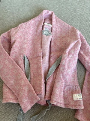 Rosa kofta Odd Molly med knytband - Mysig rosa kofta från Odd Molly med ljusgrå knytband och broderad detalj på insidan. Koftan har lång ärm, öppen front och lätt melerad struktur. Perfekt för lager-på-lager 