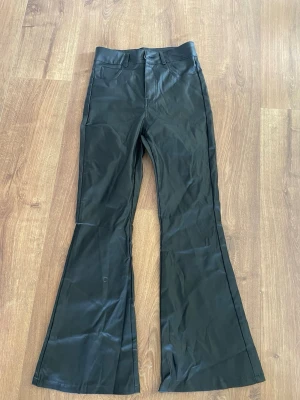 Svarta utsvängda jeans - Säljer ett par svarta jeans med utsvängda ben och klassiska fickor både fram och bak. Jeansen har hög midja och stängs med knapp och dragkedja. Materialet är  en blandning av bomull och stretch för en bekväm passform.