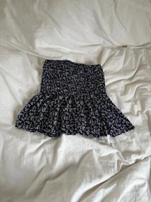 Mörkblå blommig volangkjol - Supersöt mörkblå kjol med små vita blommor och volangkant. Kjolen är jättebekväm och funkar lika bra som en tube topp om man vill det. 