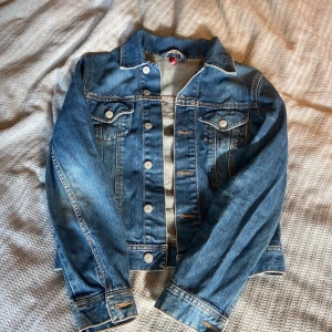 Klassisk jeansjacka från Divided - Snygg blå jeansjacka från Divided i klassisk modell med silverfärgade knappar och två bröstfickor med lock. Jackan har kontrastsömmar och är tillverkad i slitstarkt denim. Perfekt att slänga över en hoodie eller t-shirt för en chill look.