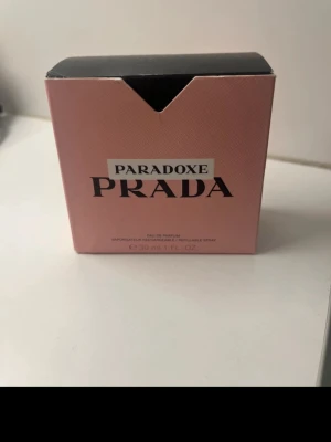 Prada Paradoxe Eau de Parfum 30ml - Prada Paradoxe Eau de Parfum i en snygg trekantig glasflaska med svart lock. Parfymen kommer i en rosa kartong och innehåller 30 ml. Flaskan har en modern design och doften är lyxig och trendig, perfekt för dig som gillar exklusiva parfymer.