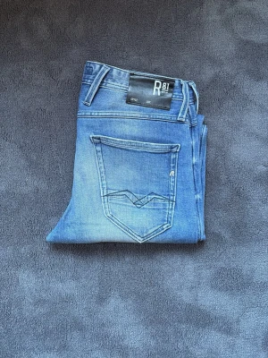 Replay anbass  - Snygga Replay Anbass jeans i klassisk blå tvätt med naturliga slitningar. Slim fit-modell som sitter bra utan att vara för tight.  Stretchigt material för hög komfort och bra passform. Perfekta till både vardag och uppklätt.  Storlek: W29/L3/ Skick: mycket bra skick!