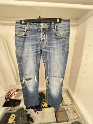 Blå slitna jeans från Jacob Cohen - Säljer ett par blå jeans från Jacob Cohen med snygga slitningar och hål på knäna. Jeansen har klassisk femficksmodell, raka ben och tydliga kontrastsömmar. Materialet är denim i bomull och bak finns en brun patch med logga. De är inte i bästa skicket, är lite känsliga vid knäna men ett snyggt par Jacob cohen för en bra peng. 