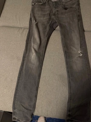 Grå dondup jeans george - Säljer ett par grå dondup jeans med slitningar på låret och knät. Jeansen har klassisk femficksmodell och dragkedjegylf. Materialet är denim med en tvättad look som ger en cool, avslappnad stil.