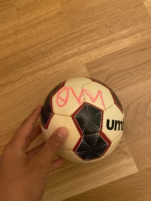 Kulusevski signerad boll  - Säljer en klassisk fotboll som är signerad av dejan kulusevski  från Umbro i vitt med svarta och röda detaljer. Bollen har ett sexkantigt mönster och är dekorerad med rosa text. Perfekt för träning eller spontanspel med vänner.
