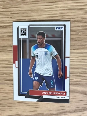 Fotbollssamlarbild Jude Bellingham - Säljer en fotbollssamlarbild från Panini Donruss Soccer Optic med Jude Bellingham i Englands landslagströja. Kortet har vita, blå och röda detaljer och visar spelaren i matchställ med nummer 8. Perfekt för dig som samlar på fotbollskort eller gillar landslagsfotboll.