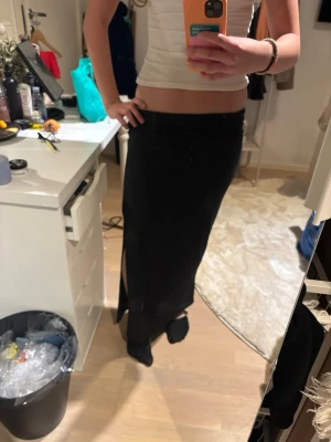 Svart långkjol från Stradivarius - Säljer en svart långkjol från Stradivarius med slits på sidan. Kjolen har en enkel och stilren design med rak passform och resår i midjan. Perfekt att matcha med crop tops eller stickade tröjor. Aldrig använt 