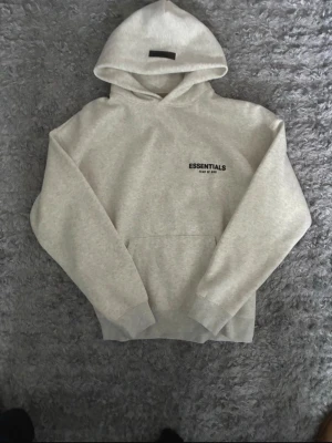  ÄKTA light oatmeal Essentials Fear of God hoodie - PASSAR BÅDE TJEJ OCH KILLEpris är it fast som sten 💯🥰 går gärna o diskutera Snygg ljusgrå hoodie från Essentials Fear of God med svart logga på bröstet. Klassisk huva, känguruficka och ribbade muddar. Perfekt för en avslappnad streetwear-look. Tillverkad i mjuk bomullsmix för maximal komfort.