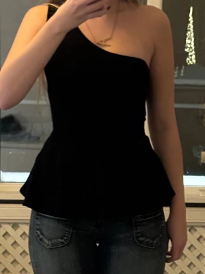 Svart oneshoulder topp - Snygg svart topp med oneshoulder-design och figurnära passform. Toppen har en volang nertill som ger en feminin touch och är perfekt att styla med jeans eller kjol. Enkel och stilren modell som passar till många tillfällen. Köpte på sellpy och kommer inte ihåg märket men den är inte från shein.