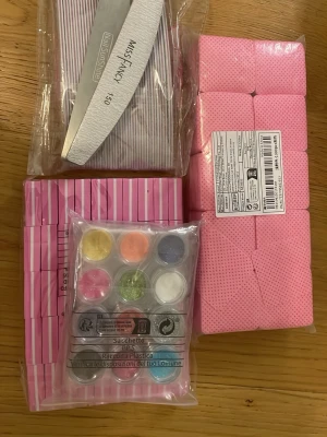 Nagelkit med filar, buffertar och glitter - Ett komplett nagelkit med vita nagelfilar från Miss Fancy, rosa nagelbuffertar och ett set med färgglada glitterpulver i olika nyanser. Perfekt för att skapa kreativa nageldesigner hemma. Allt är förpackat i separata plastförpackningar.