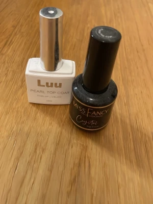 Två top coat nagellack - Säljer två top coat nagellack: Luu Pearl Top Coat i vit flaska med silverlock och Miss Fancy Professional Crystal Top Coat i svart flaska med svart lock. Båda är perfekta för att ge naglarna en snygg finish och extra glans.