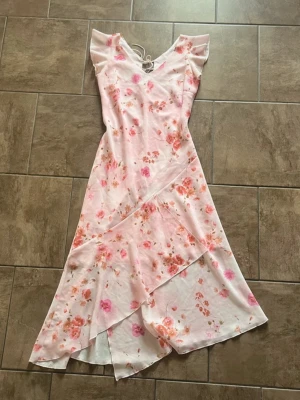 Rosa blommig midi klänning sommarklänning midsommar student bröllop volanger S/M - Jättefin ljusrosa blommig midi-klänning i romantisk och feminin stil.🌸 Smickrande passform med volanger, volangärmar och omlottdesign nedtill som ger ett fint fall. Knytdetalj baktill som gör att passformen kan justeras.  Storlek 38/M men passar mer som 36/S. Mycket bra skick. 