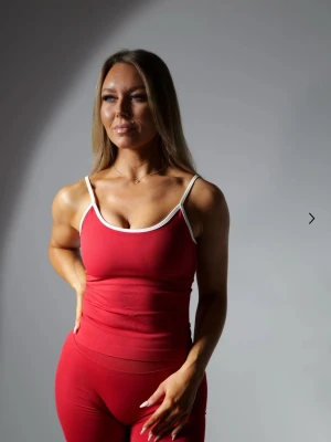 Röd sportlinne med vita detaljer från Gtech - Snyggt rött sportlinne med smala axelband och vita kanter runt hals och axlar. Perfekt för träning eller gymmet, tillverkad i stretchigt material som sitter tight och bekvämt. Inbyggd bh, endast testad en gång. Matcha med leggings för en komplett look. Nypris: 349 kr