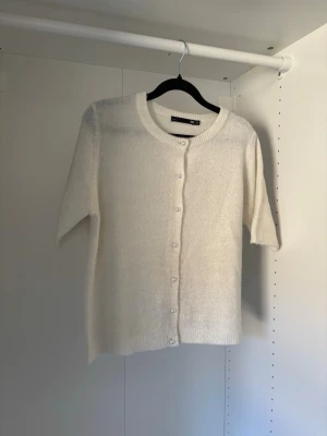 Vit kortärmad kofta - Kofta med pärlknappar, använd vid få tillfällen så i fint skick, börjar dock bli lite smått nopprig vilket syns på bilderna.