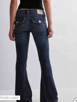 Mörkblå bootcut jeans True Religion - KONTAKTA MIG OM DU VILL HA FLERA BILDER Snygga mörkblå bootcut jeans från True Religion med kontrastsömmar och ikoniska fickdetaljer bak. Jeansen har låg midja och utsvängda ben, samt dekorativa knappar på bakfickorna. Perfekta för en trendig och avslappnad stil. Om någon är intresserad, vill se flera bilder snacka med mig på chatten.