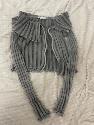 Grå ribbstickad tröja från Zara - Trendig grå ribbstickad tröja från Zara med croppad passform och långa ärmar. Tröjan har en bred krage och råa kanter för en edgy look. M i storleken men känns som S. 