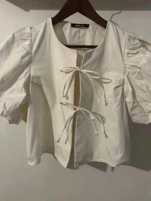 Vit puffblus med knytband från Gina Tricot - Säljer en vit blus från Gina Tricot med puffiga korta ärmar och två knytband framtill. Mycket bra skick! 