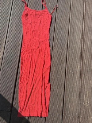 Röd långklänning från Amisu - Snygg röd långklänning från Amisu med smala axelband och figurnära passform. Klänningen är ärmlös och tillverkad i ett mjukt, ribbat material som känns bekvämt mot huden. Perfekt för varma dagar och somriga tillfällen.