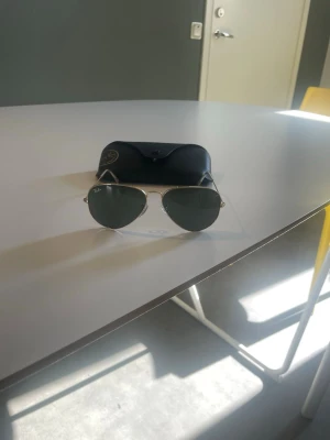 Ray-Ban aviator solglasögon guld - Klassiska Ray-Ban aviator solglasögon med tunna guldfärgade metallbågar och mörkgröna glas. Snygg och tidlös modell som passar till många stilar. Kommer med original svart fodral.