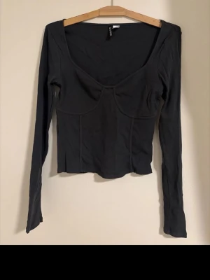 Mörkgrå långärmad topp med markerad byst - Snygg mörkgrå/mörkgrön långärmad topp med markerad byst och djup urringning. Toppen har en figurnära passform och känns mjuk och stretchig.