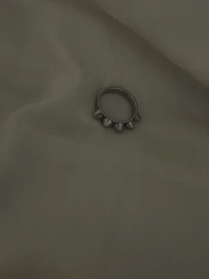 Silvrig ring med nitar - Cool ring i silverfärgad metall med flera spetsiga nitar runt hela bandet. Perfekt för dig som gillar en edgy och alternativ stil. Ringen har en rund form och är enkel att matcha med andra accessoarer.