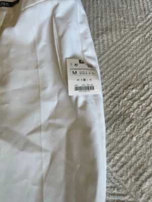 Vita kostymbyxor från Zara - Snygga vita kostymbyxor från Zara med raka ben och pressveck. Byxorna har diskreta fickor fram och är tillverkade i ett lätt, vävt material som ger en clean och fräsch look. Perfekta för dig som vill ha en stilren och modern outfit.