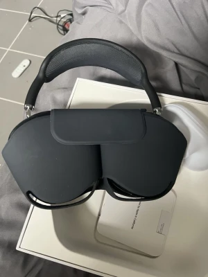Apple AirPods Max Svart Over-ear - Endast anvönda en gång Snygga svarta Apple AirPods Max over-ear hörlurar med stilren design och mjuka öronkuddar. Bygeln är vadderad för extra komfort och kåporna är i aluminium. Perfekt för dig som vill ha grymt ljud och modern look. Levereras med smart skyddsfodral.
