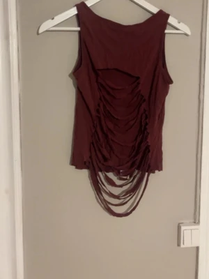 Klippt vinrött linne - Säljer ett vinrött linne från LINDEX som är klippt längst ner och i bak. Linnet är ärmlöst med rund halsringning och har en unik design. Perfekt för dig som vill sticka ut med din stil. Klippningen är dock inte så bra men går säkert att klippa till bättre om man skulle vilja. Skulle även säga att den passar både Xs och S.