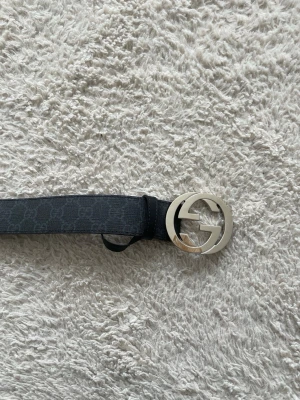 Svart Gucci skärp med silver GG-spänne - Säljer ett svart skärp från Gucci med diskret GG-mönster och ett stort, rundat silverfärgat GG-spänne. Skärpet är tillverkat i skinn och kommer med originalförpackning och påse. Perfekt för att lyfta din outfit med en ikonisk detalj.