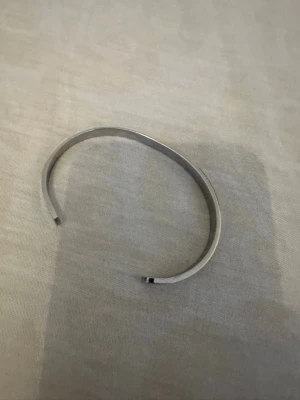 Maison Margiela silverfärgat armband - Snyggt och stilrent armband från Maison Margiela i silverfärgad metall. Armbandet är stelt och har en öppen design med ingraverad logotyp på utsidan. Perfekt accessoar för dig som gillar minimalistisk och modern stil.