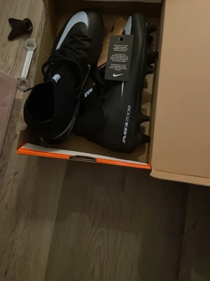 Nike Air Zoom svarta fotbollsskor - Snygga svarta Nike Air Zoom fotbollsskor med vit detalj på ovansidan och klassisk Nike-logga. Skorna har en strömlinjeformad design och högre skaft för extra stöd. Perfekta för dig som vill ha grymt grepp och stil på planen.