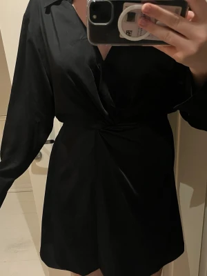 Svart omlottklänning med v-ringning - Snygg svart kortklänning med omlottdesign och v-ringning. Klänningen har långa ärmar och en Materialet är mjukt och följsamt.💞💞🙌