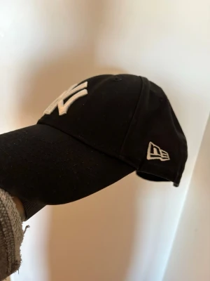 Original New Era New York Yankees keps - oanvänd  - Säljer en original New Era New York Yankees keps i svart med vitt broderat Yankees-logo.   Det är en youth/junior-modell, alltså för barn/ungdom och inte vuxenstorlek.                                                   Skick: Oanvänd, mycket fint skick.   Färg: Svart med vit logga.   Märke: New Era.   Modell: New York Yankees / MLB.   Storlek: Youth.