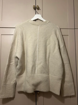 beige stickad tröja - beige stickad tröja med passform och breda ribbade muddar vid ärmslut och nederkant😍tröjan har en markerad söm som löper vertikalt framtill och baktill, samt rund halsringning