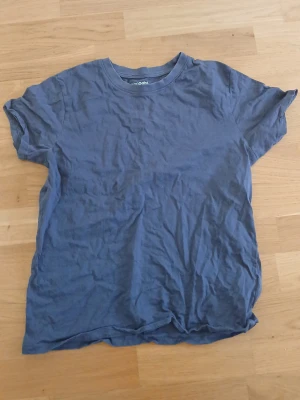 Grå t-shirt  - En enkel grå t-shirt från kappahl med rund halsringning och korta ärmar. Tillverkad i mjuk bomull och har en avslappnad passform. Perfekt för en chill och stilren look. Stryks innan skickning så den kommer stilig till en. Storlek 158/164. Den ser blå ut men är grå.