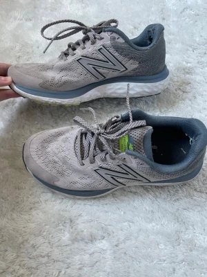 Grå New Balance sneakers mesh - Snygga grå sneakers från New Balance med ventilerande mesh-ovandel och klassisk N-logga på sidan. Skorna har snörning, vadderad häl och en bekväm, stötdämpande sula. Perfekta för dig som gillar sportig och stilren look. Finns lite slitningar vid inne vid hälen, se bilderna. Annars fint skick! 