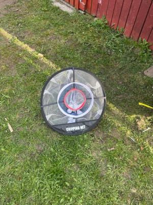 Golf chipping-nät med bollar - Golf chipping-nät i svart och vitt med färgade ringar och flera vita plastbollar. Perfekt för att träna precision i trädgården eller på gården. Nätet är hopfällbart och lätt att ta med sig.