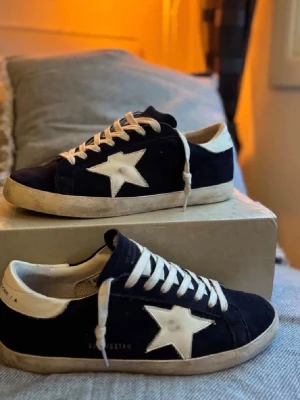 Mörkblå Golden Goose sneakers med stjärna - Snygga svarta sneakers från Golden Goose med vit stjärndetalj på sidan och vita skosnören. Skorna har en låg profil och vit sula med vintage-look. Perfekta för en cool och avslappnad stil.