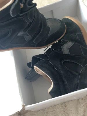 Svarta Isabel Marant wedge sneakers - Snygga svarta wedge sneakers från Isabel Marant med högt skaft och kardborreband. Skorna är i mocka och har detaljer i läder samt en beige sula. Perfekta för dig som vill ha en cool och trendig look med extra höjd.