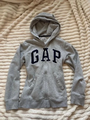 Grå hoodie med dragkedja GAP kids - En grå hoodie med dragkedja ifrån GAP kids i storlek 14-16 år, passar som en xs eller xxs! Defekter som nopprig, urtvättad kan förekomma. En defekt är en liten fläck vid axeln som syns på bilden! Tar prisförslag❣️