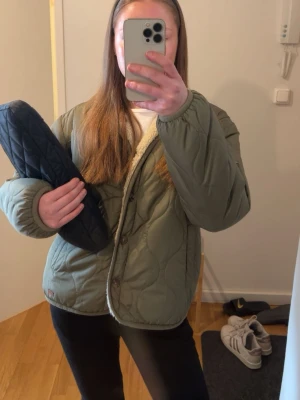 Olivgrön quiltad jacka - Säljer en olivgrön quiltad pufferjacka med knäppning framtill och två fickor. Jackan har en mysig beige fuskpäls på insidan och en oversized passform. Perfekt för kalla dagar och riktigt skön att bära. Passar dig som gillar en avslappnad och trendig stil.
