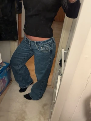 Blåa baggy jeans med låg midja - Säljer ett par blåa baggy jeans med extra låg midja och raka, vida ben. Jeansen har klassiska fickor fram och bak samt en cool detalj på bakfickan. Perfekta för en avslappnad och trendig look. Materialet är klassisk denim i bomull.