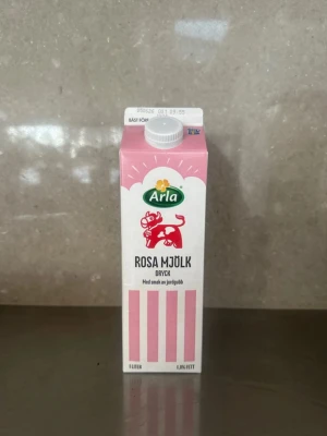 Arla Rosa Mjölk jordgubb 1L - En 1-liters förpackning Arla Rosa Mjölk dryck med smak av jordgubb. Kartongen är vit och rosa med ränder och har en röd ko på framsidan. Perfekt för dig som gillar smaksatt mjölk och vill ha något annorlunda till frukost eller mellis.