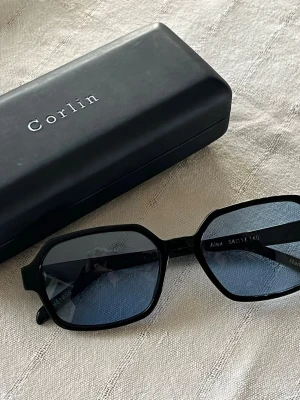 Svarta solglasögon från Corlin - Alex black blue från Corlin. Nypris 1299. Sparsamt använda.  CR39-linser ger klarhet och reptålighet  Fullständigt UV400-skydd blockerar 100 % av UVA- och UVB-strålar. 