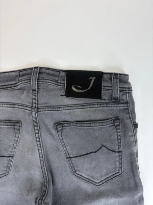 Grå slim fit jeans från Jacob cohen - Snygga grå slim fit jeans från Jc med klassiska fem fickor och svarta detaljer. Jeansen har en stilren tvätt och är tillverkade i bomullsblandning med stretch för extra komfort. Perfekta för en trendig och avslappnad look.