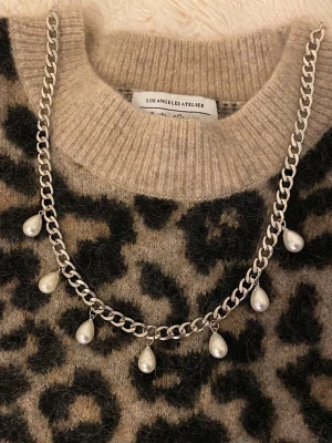 Silverfärgat halsband med pärldroppar - Snyggt halsband i silverfärgad rostfritt med sju droppformade vita pärlor som hänger längs kedjan. Kedjan är grov och ger ett trendigt intryck. Perfekt accessoar för att lyfta din outfit med en cool och elegant touch.
