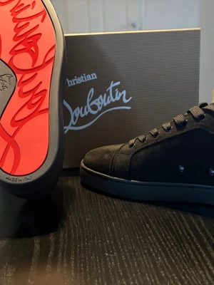 Svarta Christian Louboutin - Stilrena svarta sneakers från Christian Louboutin i mocka med klassisk röd sula och svarta skosnören. Snygg och minimalistisk design med diskreta nitar på sidan och ikonisk signatur under sulan. Perfekta för dig som vill ha något exklusivt och trendigt. Skriv dm vid intresse, kan gå ner i pris