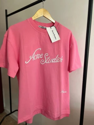 Rosa Acne Studios t-shirt med logga - Snygg rosa t-shirt från Acne Studios med vit broderad logga framtill. Klassisk passform med nypris 3800 kr 