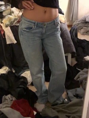 Ljusblå raka jeans med låg midja - Säljer ett par ljusblå jeans med rak passform och låg midja. Klassisk femficksmodell med dragkedja och knapp framtill. Perfekta för en avslappnad och trendig look. Materialet är denim i bomull.