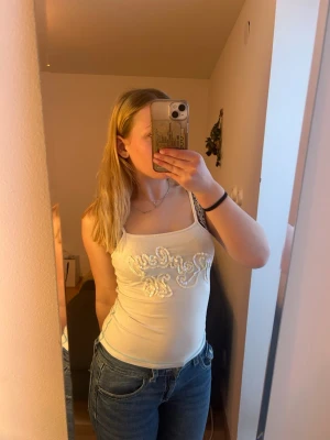 Vit paljettlinne från Replay - Säljer ett vitt linne från Replay med tunna axelband och paljetter i ett snyggt mönster framtill. Perfekt till jeans eller kjol för en trendig och fräsch look. Materialet är mjukt och stretchigt för skön passform.